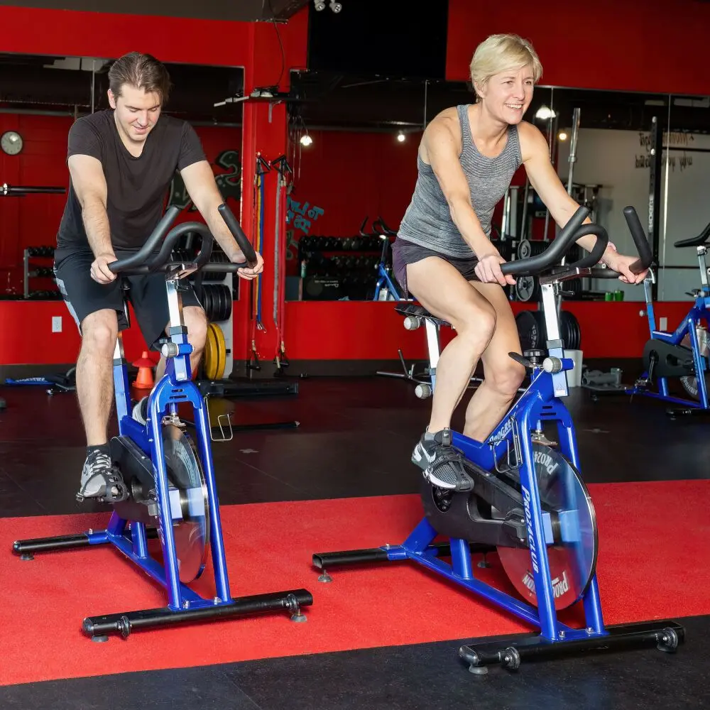 Fit young man and healthy middle aged woman ride their spin cycles at a group cardio class